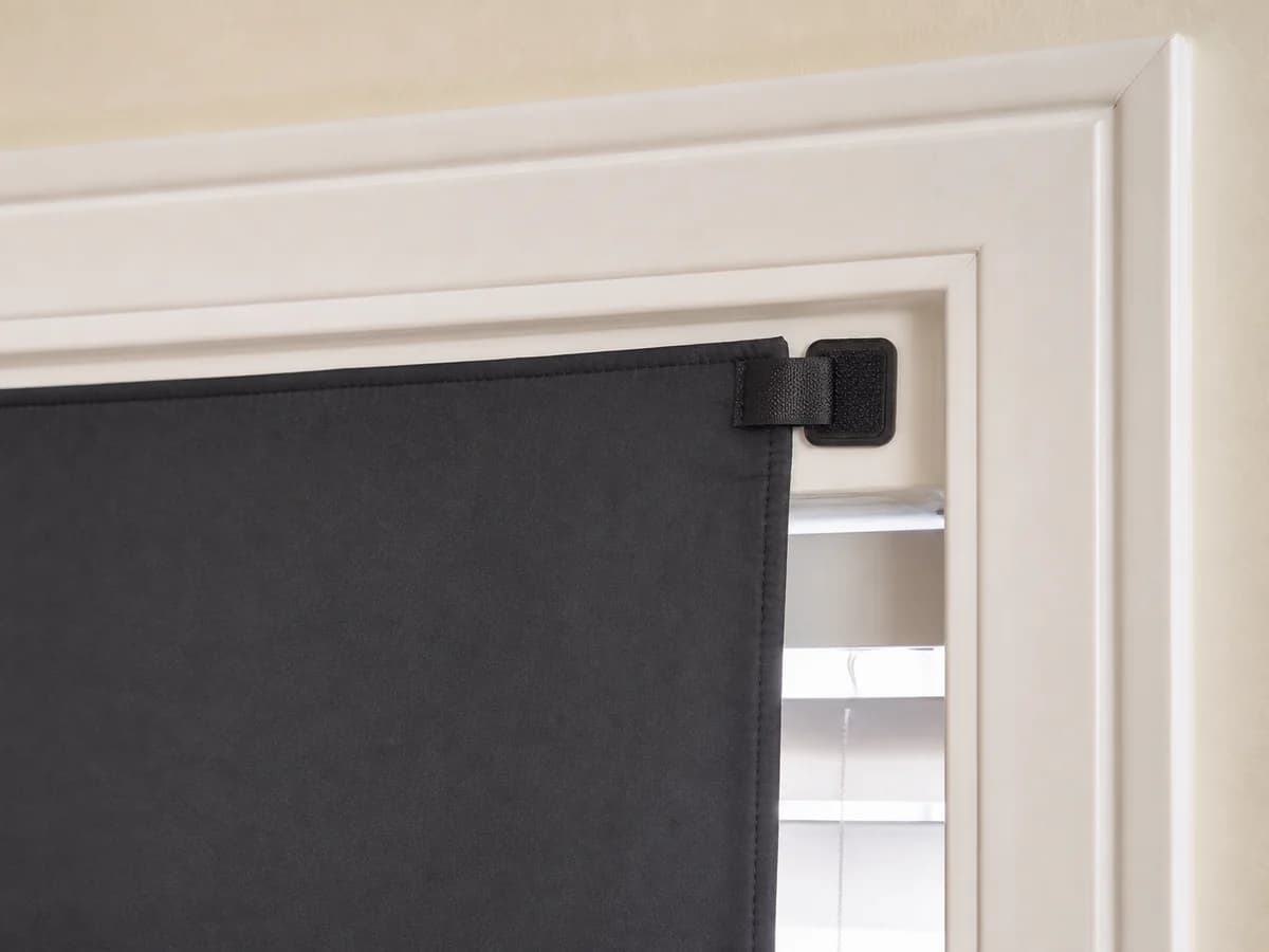 Corner of a removable full-window blackout panel attached to a smooth window frame without covering the hardware.